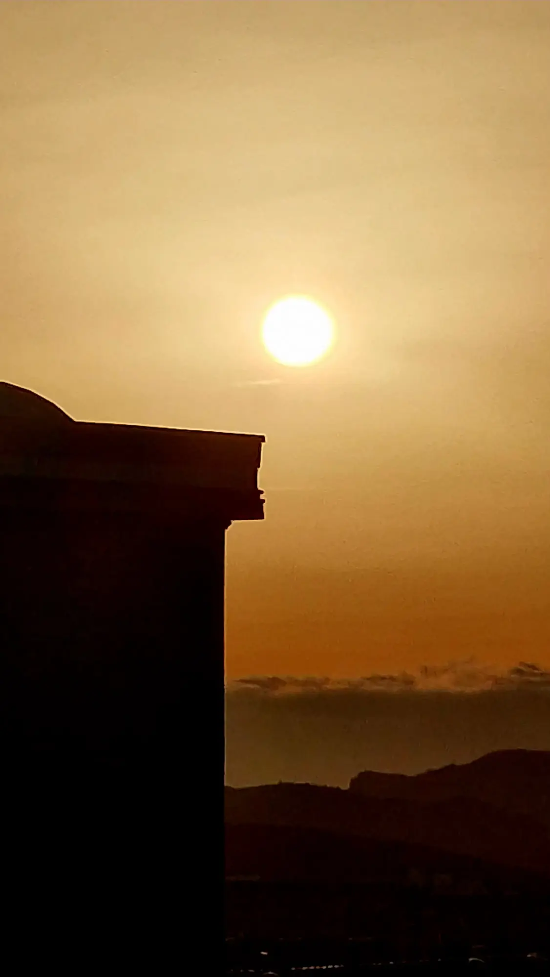 Sol sobre la silueta de un edificio en un cielo dorado